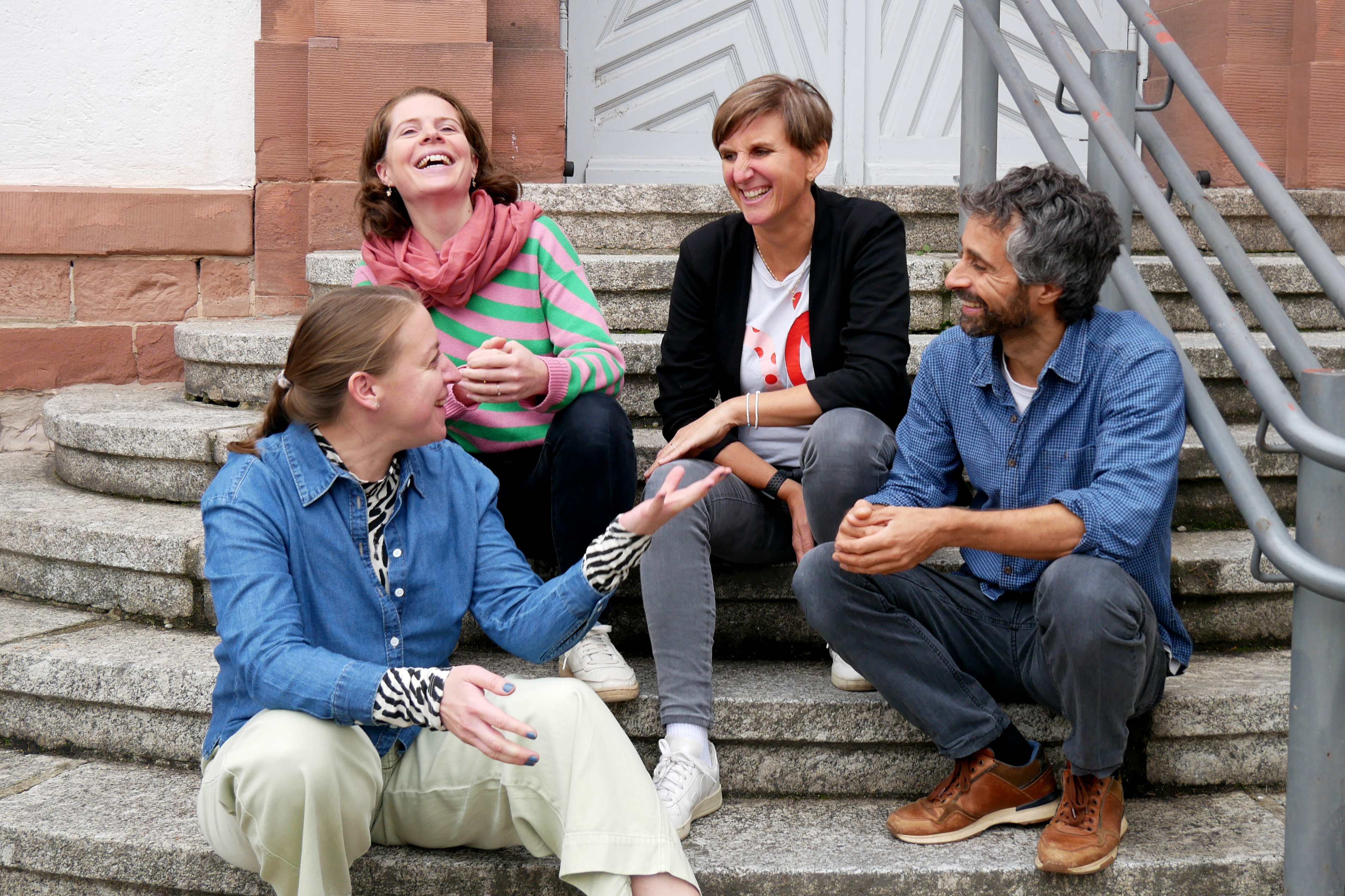 Fachrichtung Sprache Vier Ausbilder:innen der Fachrichtung Sprache sitzen auf der Steintreppe am Seminareingang und unterhalten sich.