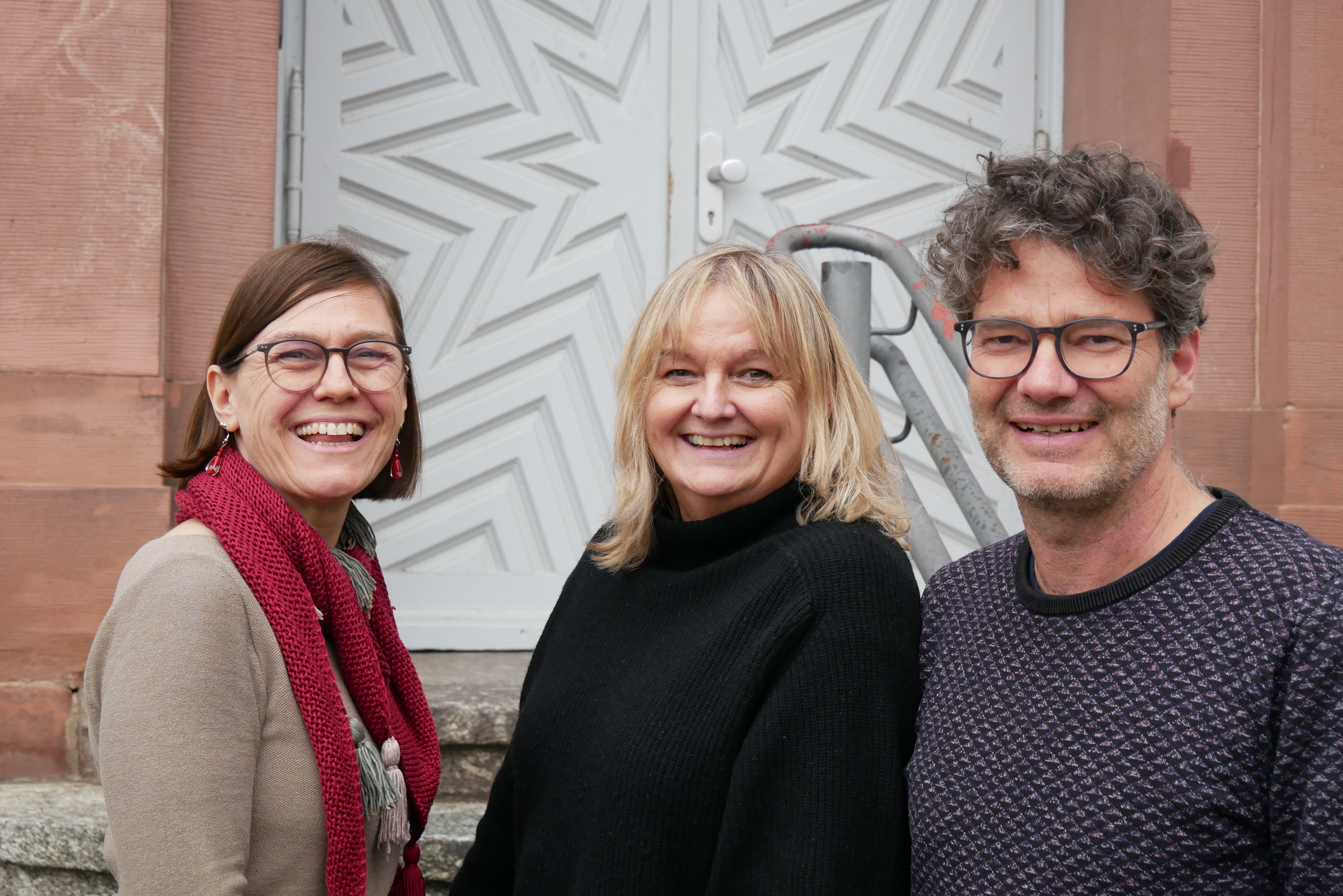 Die drei Ausbilder:innen der Fachrichtung KMENT stehen vor der Eingangstüre des Seminars.